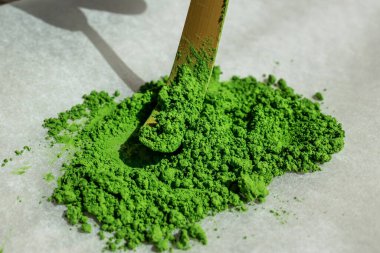 Canlı yeşil kibrit çay tozu, geleneksel bambu çatal bıçakla kepçeleniyor, ince dokusunu ve zengin rengini sergiliyor, mutfak ve törensel amaçlar için ideal..