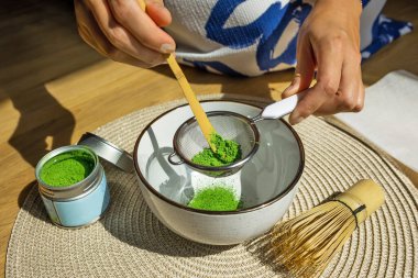 Bir kişi, geleneksel süreci ve canlı yeşil rengi gösteren süzgeç ve bambu çırpıcı kullanarak kibrit çayı hazırlar..