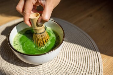 Japon kültürünü ve geleneğini temsil eden canlı yeşil kibrit çayını köpürtmek için bambu çırpısı kullanan bir el. Çay, çay yapma sanatını ön plana çıkaran seramik bir kasede hazırlanır..
