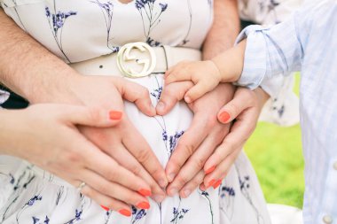 Aile üyeleri hamile bir karında kalp şekli oluşturuyorlar. Aşkı, birliği ve beklentiyi simgeliyorlar. aile anları.