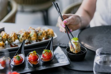 Bir el lezzetli bir suşi rulosu almak için çubuk kullanır, güzel kaplanmış Asyalı aperatiflerle çevrili..