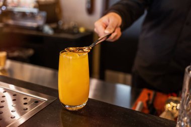 Bir barmen ustalıkla ferahlatıcı bir narenciye kokteyli hazırlar, üstüne garnitür olarak ızgara dilimi koyar, şık bir barda miksoloji sanatını yakalar..