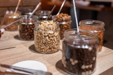 Cam kavanozlarda kaşıklarla sergilenen çeşitli fındık ve kurutulmuş meyveler. Ahşap masa düzenleme, beslenme ve organik gıdalar..