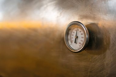 Metalik bir yüzeye monte edilmiş endüstriyel bir termometreye yakın çekim. Sıcaklığı Celsius derecesinde gösteriyor. Görüntü endüstriyel bir ortamda kesinlik, mühendislik ve sıcaklık ölçümünü vurgular.