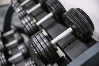 Spor salonundaki ağırlık askısına düzgünce yerleştirilmiş ağır dambıllara detaylı bir bakış. İspatlama fitness, dayanıklılık eğitimi ve sağlıklı bir yaşam tarzı..