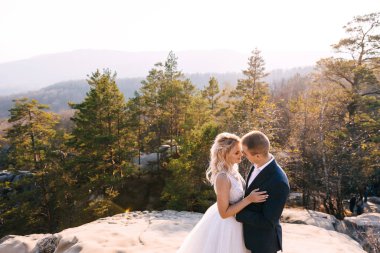 Gelin ve damat bir uçurumun üstünde duruyorlar. Gün batımı.