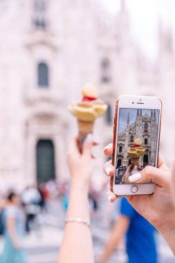 Telefon ekranına yakın çekim ve Milan Katedrali Duomo 'nun arka planında dondurmayla el fotoğrafı çeken kız..