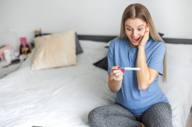 Pozitif hamilelik testinden sonra mutlu olan genç bir kadın. Güzel, sevgi dolu bir dişi yatakta müstakbel ebeveyn olacağı için mutlu ve heyecanlı hisseder. Aile Bekleyen Bebek Konsepti