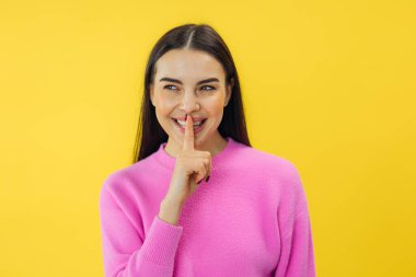 Sevimli, sevimli, çekici kadın sarı arka planda izole edilmiş sessiz bir jest yapıyor.