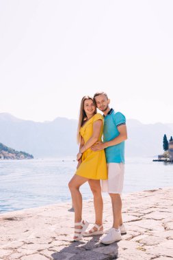 Neşeli bir çift güneşli bir yaz gününde sahile poz verir, neşe ve sevgi saçarak deniz kenarının parlak ve sakin çevresini tamamlayan canlı giysiler sergilerler..