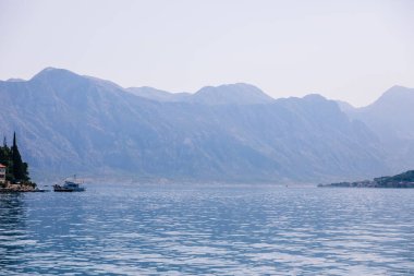 Fotoğraf, berrak bir su kütlesinin yanında huzurlu bir dağ manzarası yakalıyor. Küçük tekneler huzurlu bir yolculuk ve tatil ortamı yaratıyor..