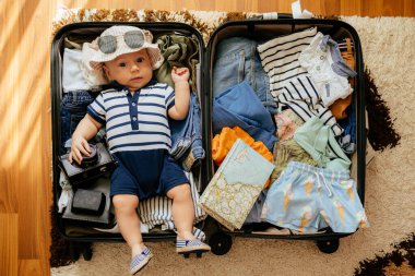 Güzel erkek bebek valizde yatıyor. Eşyaları ve giysileri var. Arka planda mesaj için yer var.