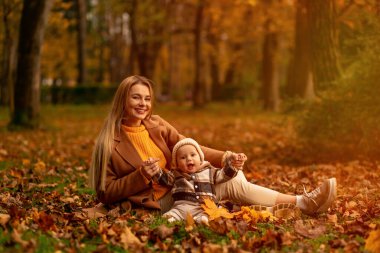 Bir anne ve çocuğunun iç açıcı bir görüntüsü. Açık havada, canlı sonbahar yaprakları arasında eğleniyorlar. Aile sevgisini ve mevsimsel neşesini sergiliyorlar..