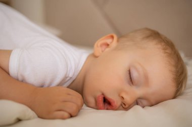 Huzurlu beyaz bir yatakta huzur içinde uyuyan bir bebeğin rahat ve rahat bir ortamda huzurlu ve sakin bir dinlenme ve masumiyet atmosferi yayması..