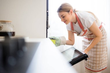 Bir kadın açık fırının önünde önlükle diz çöker, pişirmek için bir şeyler hazırlar. Sıcak, ev yapımı atmosfer ev yemeği ve pişirme için ideal..