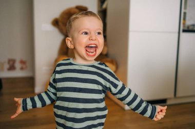 Sıcak bir evde kollarını açarak sevinç ifade eden neşeli bir çocuk..