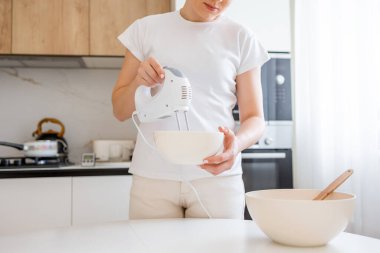 Bir insan modern mutfak ortamında hamuru hazırlamak için bir el mikseri kullanır..
