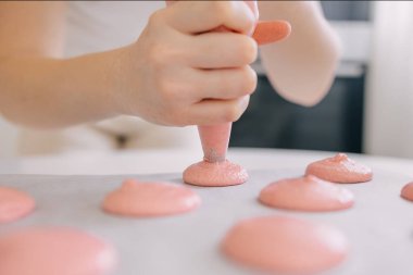 Ellerin yakın çekim görüntüsü, pipo torbasıyla pişirme tepsisinde pembe badem kurabiyesi hamuru oluşturması..