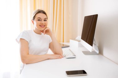 Elektrik ayarlanabilir bir masada oturan mutlu bir birey iyi ışıklandırılmış bir ofis ortamında, bilgisayar kullanıyor. Uzak çalışma için uygun organize ve üretken çalışma ortamı.