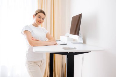 Elektrikli bir masada kendine güvenen bir kadın. Parlak ve düzenli bir ofis ortamında çalışıyor. Rahat ve verimli bir çalışma alanı için üretkenlik ve uygun ergonomik.