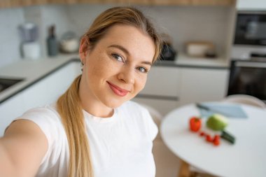 Taze sebzelerle çevrili, modern ve parlak bir mutfakta poz veren bir kadın. pozitif ve mutlu, yemek pişirme, sağlık ve rahat bir ev ortamı.