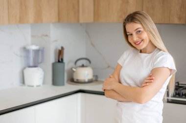 Neşeli bir kadın aydınlık, modern bir mutfakta yemek pişiriyor..