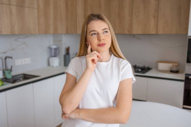 Modern bir mutfakta düşüncelere dalmış genç bir kadın. Temiz ve modern bir mutfak ortamında geçen ilham ve farkındalık..