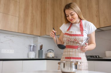 Modern mutfak ortamında yemek pişiren önlüklü bir kadın sağlıklı beslenme alışkanlıkları ve ev yapımı yemekler hazırlamanın keyfi. Evde mutlu ve rahat yemek pişirme deneyimi.