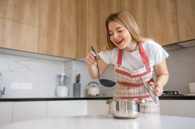 Sıcak mutfağında kepçeyle önlük çorbası içen neşeli bir kadın..