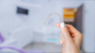Çağdaş ortodontik teknolojiyi ve diş bakımını sembolize eden diş ortamında bir el tarafından tutulan şeffaf bir ortodontik hizalayıcının yakın çekimi.