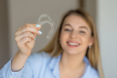 Neşeli bir kadın, diş bakımı, diş sağlığı ve modern kozmetik dişçiliği için çözümleri düzelten görünmez dişleri vurgulayan bir dizi temiz diş düzenleyicisi tutuyor..
