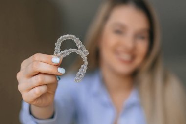 Şeffaf diş hizalayıcılarını gösteren neşeli bir kadın, diş bakımını ve ortodontik tedavi çözümlerini vurgulayarak gülümsemeleri ve ısırık hizalarını artırmaya çalışıyor..