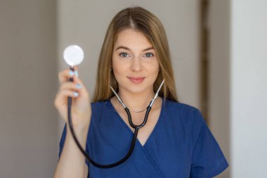 Kendine güvenen genç bir sağlık uzmanı içeride duruyor, önlük giyiyor ve steteskop tutuyor. Sağlık, konfor ve tıbbi uzmanlığın teşvik edilmesi.