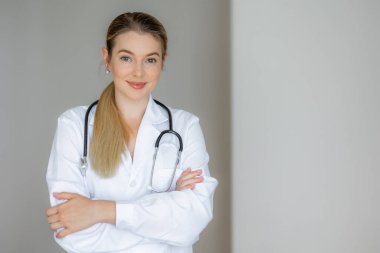 Tıbbi giysiler ve steteskop giymiş, kollarını kavuşturmuş kendine güvenen bir kadın doktor..