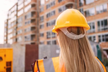 Güvenlik kaskı takmış bir kadın işçiye odaklanmış bir inşaat alanı. Gelişmekte olan bir şehir binasının önünde dikiliyorum.  