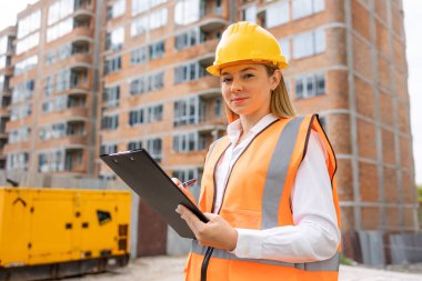 Güvenlik kaskı ve yelek giyen kadın bir inşaat işçisi inşaat çalışmalarını inceliyor.. 