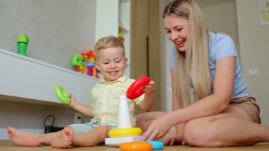 Bir anne ve küçük oğlunun hoş bir odada renkli oyuncak bloklarıyla piramit inşa ettiği neşeli bir sahne.. 
