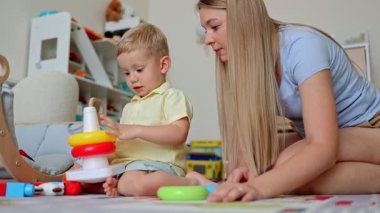 Bir anne ve küçük oğlunun hoş bir odada renkli oyuncak bloklarıyla piramit inşa ettiği neşeli bir sahne.. 