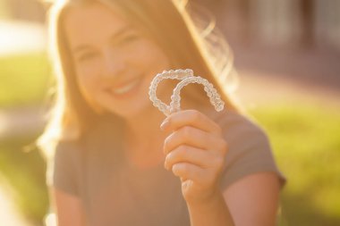 Neşeli bir kadın, elinde güneş ışığı, diş bakımını, ortodontik düzeltmeyi ve kendine güveni sembolize ederken gülümsüyor. Sağlık ve güzelliğin iyimser ve olumlu teması.
