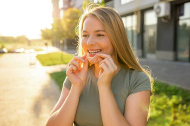 Açık havada güneşli bir ortamda ortodontik dizilim kullanan genç bir kadın. Mükemmel bir gülümsemeye ulaşmak için çözümler.