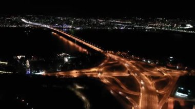 Ukrayna, Kyiv 'deki Paton Köprüsü. Hava görüntüsü. Köprüde trafik var. Arabaların dairesel hareketi. Gece. 