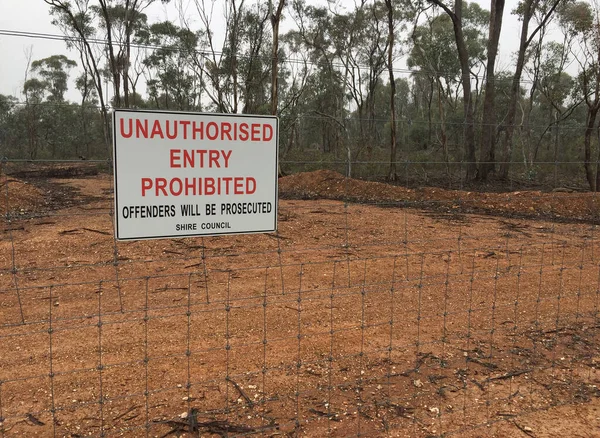 a red, black and white Unauthorised Entry Prohibited, Offenders Will Be Prosecuted sign on the fence of shire council property