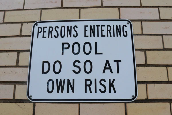黒と白の人がプールに入ると クリームレンガの壁に自分のリスク警告サインでそうします — ストック写真