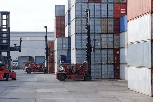 Forklift trucks handling freight, container boxes in logistic delivery yard with stacks of cargo containers.