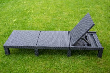 Çimlerin üzerinde plastik bir açık hava rattan yatağı.