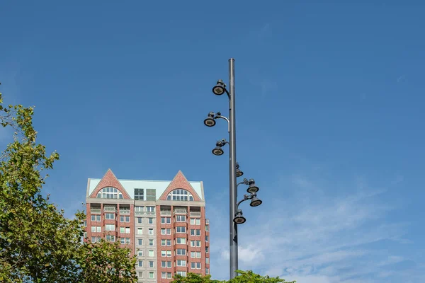 Modern residential building and led lighting on a pole. Blue sky and green branch