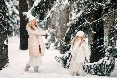 Yakışıklı anne ve kız kışın dışarıda eğleniyorlar. Karlı ağaçlar arasında ormanda karla oynamak