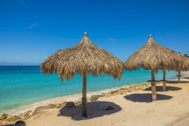 Güneş yatakları, kumlu sahildeki şemsiyeler turkuaz su yüzeyi ve mavi gökyüzü arka planı. Aruba. 