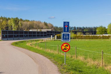 Yol kenarındaki tabelaların görüntüsü. Arka planda yeşil ağaçlar ve mavi gökyüzü. İsveç. 