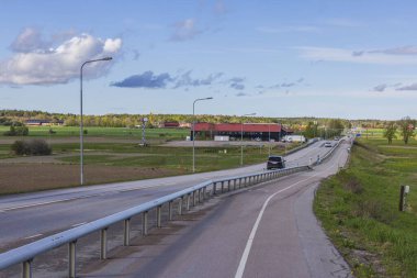 Aydınlık bir günde güzel bir kır manzarası. Asfalt yolu ve mavi gökyüzü arka planında yeşil alanlar. İsveç. 